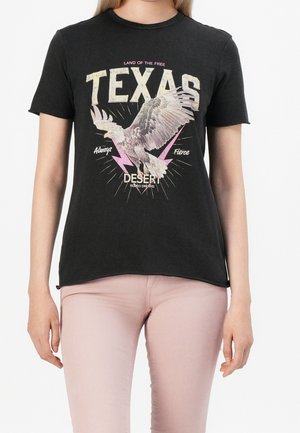 Camiseta negra de algodón con texto gráfico "TEXAS", diseño de águila y acentos de relámpagos rosas. Mangas cortas y un ajuste relajado.