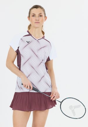 Kvinde i sportstøj, der holder en badmintonketsjer, iført en mønstret hvid og mørkerød skjorte med en mørkerød plisseret nederdel.
