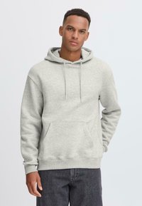 Light gray hoodie made of soft fabric, featuring a kangaroo pocket, drawstrings, and ribbed cuffs, paired with dark jeans.