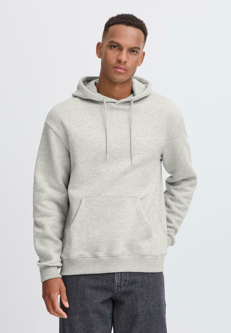 Lys grå hettegenser laget av myk stoff, med kengurulomme, snorstrikk og ribbestrikkede mansjetter, sammen med mørke jeans.
