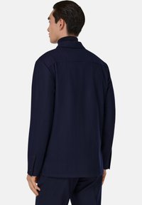 Mörkblå långärmad skjorta med hög krage, slätt tyg och knappade manschetter. Har en yoke-seam över ryggen.