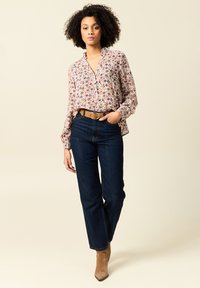 Blumenbluse mit langen Ärmeln und Kragen, kombiniert mit dunkelblauen High-Waist-Jeans und beigen Ankle Boots. Brauner Gürtel mit Schnallendetails.