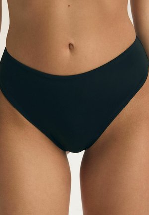 Zbliżenie osoby noszącej czarne bikini z wysokim stanem, pokazujące dolną część tułowia i górne partie ud na jednolitym tle.