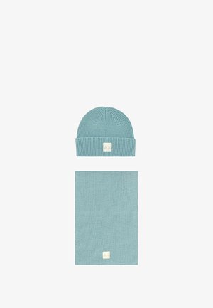 Berretto in maglia blu con risvolto e un'etichetta, abbinato a una sciarpa rettangolare coordinata. Entrambi gli articoli presentano un motivo testurizzato.