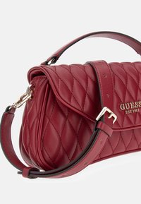 Rode gewatteerde leren handtas met bovenhandvat, verstelbare schouderriem, goudkleurige gesp en "GUESS EST 1981" logo op de voorklep.