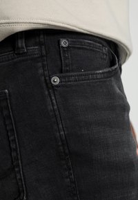 Calças de ganga pretas com corte justo, textura desbotada, detalhes em metal e um bolso para moedas do lado direito.