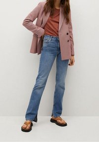 Vaaleanpunainen ruudullinen bleiseri ruosteenvärisen topin päällä, yhdistettynä sinisiin suoralahkeisiin farkkuihin ja mustiin korokepohjaisiin varvassandaaleihin.