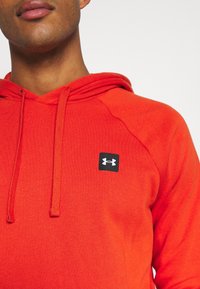 Felpa con cappuccio rossa realizzata in tessuto morbido, dotata di tasca a marsupio e caratterizzata da un piccolo logo Under Armour nero sul petto.