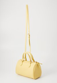 Borsa a mano in pelle gialla con forma rotonda strutturata, doppio manico superiore, tracolla regolabile e dettagli in metallo dorato. Finitura texturizzata.