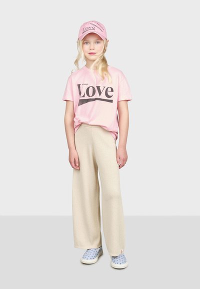 Ružičasta pamučna majica s grafikom "Always Love", bež široke hlače i svijetloplave slip-on cipele s uzorkom, upotpunjene odgovarajućom kapicom.