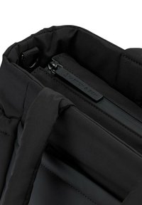 Musta kangaskassi, jossa on pehmustettu sisustus ja sivuzipperi. Varustettu sileillä, teksturoiduilla kahvoilla ja merkkitarralla sisällä.