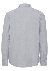 Chemise à manches longues rayée en blanc et bleu marine, dotée d'un col et de poignets à boutons, avec des rayures verticales et une texture lisse.