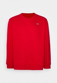 Czerwona bluza z długim rękawem, wykonana z bawełny, z okrągłym dekoltem i ściągaczami, z małym zielono-białym logo na piersi.