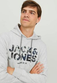 Sudadera gris con capucha, con cordón, gran logo de la marca en diseño de camuflaje, textura suave y puños de canalé. Corte casual con un bolsillo tipo canguro.