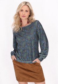 Sötétkék, hosszú ujjú ing, ami zöld és piros paisley mintázattal rendelkezik, barna velúr mini szoknyával párosítva.