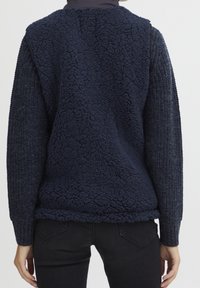 Námořnický fleecový pulover s texturovanými tkanými rukávy, který má měkký chlupatý zadní díl a žebrované manžety pro větší teplo a pohodlí.