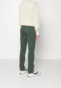 Gröna bomullshängslen med slim fit, kontrasterande bakficka, som är parat med vita sneakers med färgade detaljer i rött och teal.