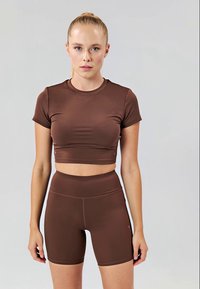 Haut court ajusté marron et short taille haute en matériau lisse et extensible. Présente des manches courtes et un col rond simple.
