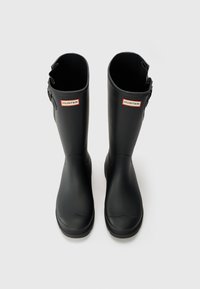 Bottes de pluie en caoutchouc noir avec une finition mate, bout arrondi, détail de boucle sur le côté et un logo de marque rouge et blanc en haut.