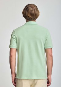 Mintgrön polo med kort ärm, krage och sidenickar i fållen. Slät textur och avslappnad design.