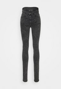 Jeans skinnies de talle alto en negro con lavado ácido, con dos bolsillos traseros y detalles de costura, mostrados desde la parte trasera.