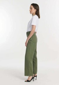 Groene wijde broek met voor- en achterzakken, hoge taille en contrasterende stiksels, gecombineerd met een wit T-shirt en zwarte hakken.
