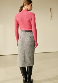 Fitted ribbestrik kravebluse i pink, parret med en knælang grå herringbone-nederdel. Sorte knæhøje læderstøvler fuldender looket.