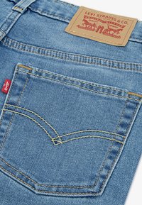 Blugi din denim albastru cu un buzunar spate cusut cu aţă galbenă și o etichetă de piele pe talie inscripționată cu "LEVI STRAUSS & CO.".