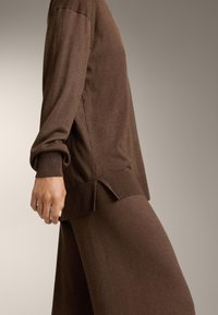 Barna kötött pulóver hosszú ujjal, bordázott mandzsettákkal, oldalszínekkel és laza illeszkedéssel, puha, texturált anyagból készült.