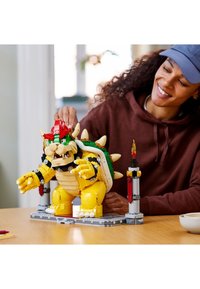 LEGO Bowser model in yellow and green with red accents. Features spiked shell, claws, and a base with light-up elements.