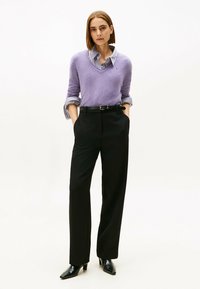 Suéter lila con un escote en pico profundo, superpuesto a una camisa de cuello azul y blanca a rayas. Pantalones negros ajustados y tacones negros de punta.