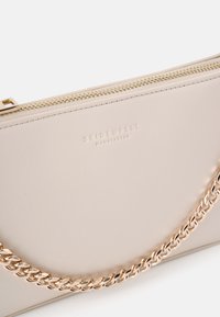 Beige Lederhandtasche mit goldfarbenem Kettenriemen und Reißverschluss, mit geprägt wirkendem Logodetail auf der Vorderseite.
