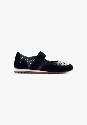 Zapato deportivo plano para mujer negra con recortes triangulares, correa de velcro, detalles en ante, entresuela blanca y suela exterior marrón estriada.