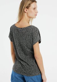 Camiseta de estampado de leopardo gris con mangas cortas, escote amplio y textura suave. Bajo curvado, ajuste holgado y un brillo sutil.