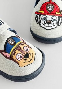 Kinderschuhe aus hellgrauem Stoff mit bestickten Cartoon-Hundegesichtern, einer trägt einen blauen Polizeihut und der andere einen roten Feuerwehrhelm.