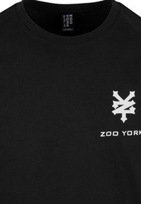Juodas medvilninis marškinėliai su apvalia iškirpte. Yra baltas "ZOO YORK" logotipas ir geometrinis dizainas kairiajame krūtinės šone. Dydis: didelis.