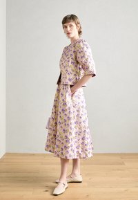 Abito stampato floreale in lavanda, con maniche corte, un corpetto corto e una gonna midi ampia. Abbinato a ballerine beige chiaro.