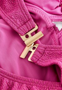 Roze stof met een gestructureerde afwerking, voorzien van gouden hardware sluitingen en gedetailleerde, elastische banden. Glad achtergrondoppervlak.
