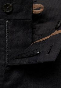 Black fabric with a textured finish features a zipper pocket and a brown fabric accent. Closure includes a black button.