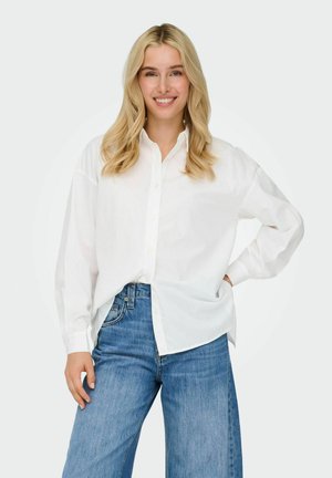 White long-sleeve shirt with button-down front, relaxed fit, layered over blue wide-leg jeans. Smooth fabric with visible button detailing.