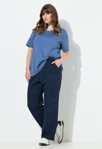 Top blu corto a maniche svelte abbinato a pantaloni texture navy con un motivo geometrico e sneakers bianche con dettagli grigi.