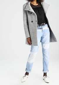 Szary teksturowany płaszcz z dużymi klapami, czarna bluzka, jeansy w patchworku w jasnym niebieskim kolorze oraz białe buty, uzupełnione rajstopami w okrągły wzór.