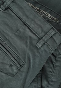 Pantalones chino de algodón verde con una textura suave, que presentan un bolsillo frontal, detalles de costura y una etiqueta que indica "algodón premium".