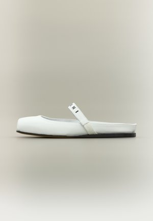 Chaussure plate blanche à bout arrondi, en cuir lisse, avec une bride élastique et un logo, semelle noire. Design simple et minimaliste.