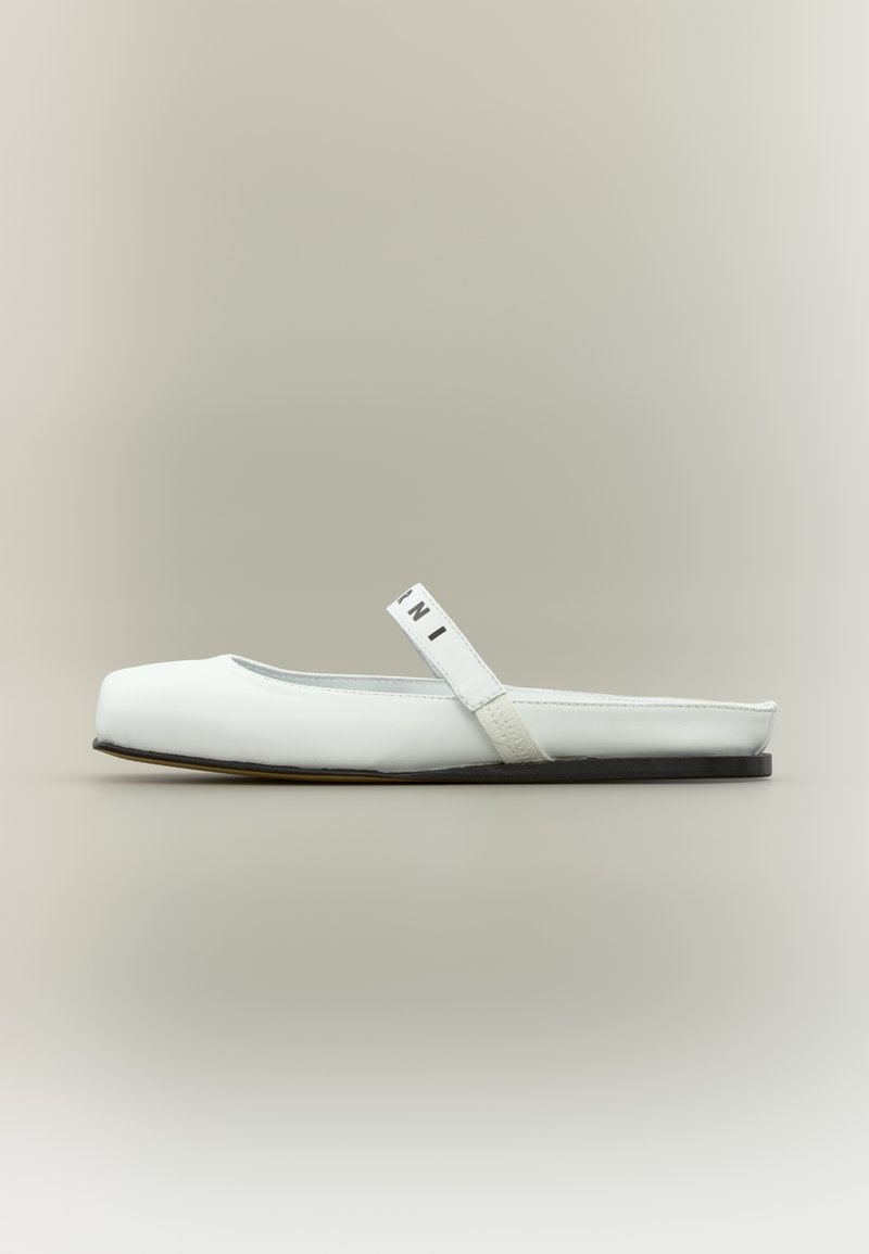 Λευκό επίπεδο παπούτσι με στρογγυλή μύτη, λείο δερμάτινο υλικό, ελαστικό λουράκι με λογότυπο και μαύρη σόλα. Απλός και μινιμαλιστικός σχεδιασμός.