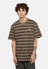 Camiseta a rayas marrón y negra con cuello redondo, mangas cortas y un parche del logo en el lado izquierdo del pecho; la tela parece suave con una textura lisa.
