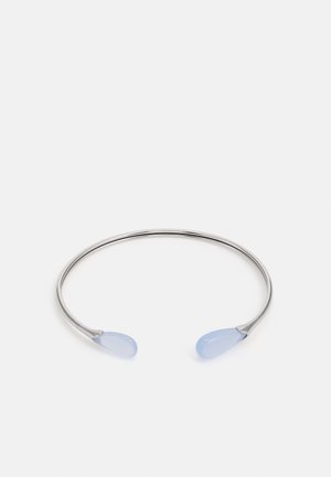 Bracelet manchette ouvert en argent avec des extrémités en pierre bleu pâle, lisses et arrondies, sur un fond blanc uni.