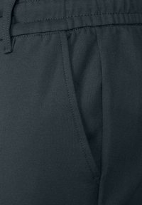 Pantalones de tela gris oscuro con una textura suave, cinturilla elástica y un bolsillo lateral con suturas sutiles.