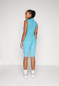 Ένα εφαρμοστό αμάνικο τοπ σε ανοιχτό μπλε απόχρωση με γιακά, συνδυασμένο με αντίστοιχες βερμούδες, και τα δύο φτιαγμένα από απαλό ύφασμα. Τα λευκά παπούτσια και οι κάλτσες μέχρι τον αστράγαλο ολοκληρώνουν την εμφάνιση.