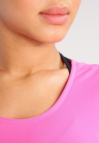 Primo piano del collo e del mento di una persona che indossa una maglietta rosa brillante con scollatura rotonda, mostrando una pelle liscia e un colore delle labbra morbido.